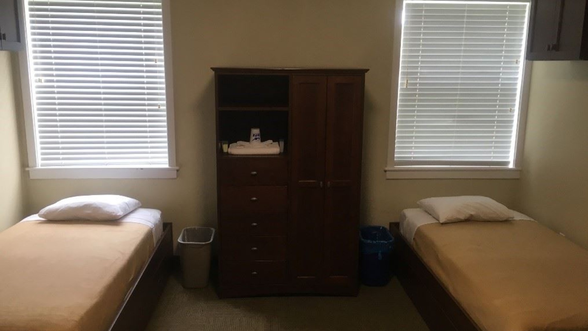 Inside a Bishops Hall Double room. There are two beds with windows above each and an armoire between the beds.