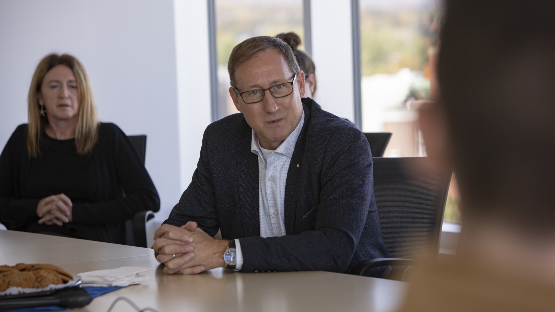 A man in a suit sitting at a table talking with two women