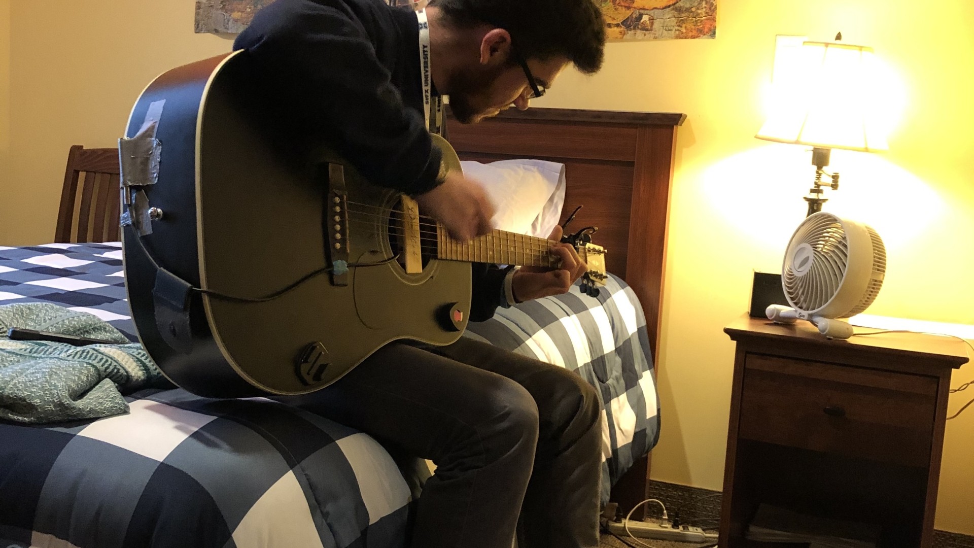 Student playing guitar while sitting on their bed in Riley Hall.