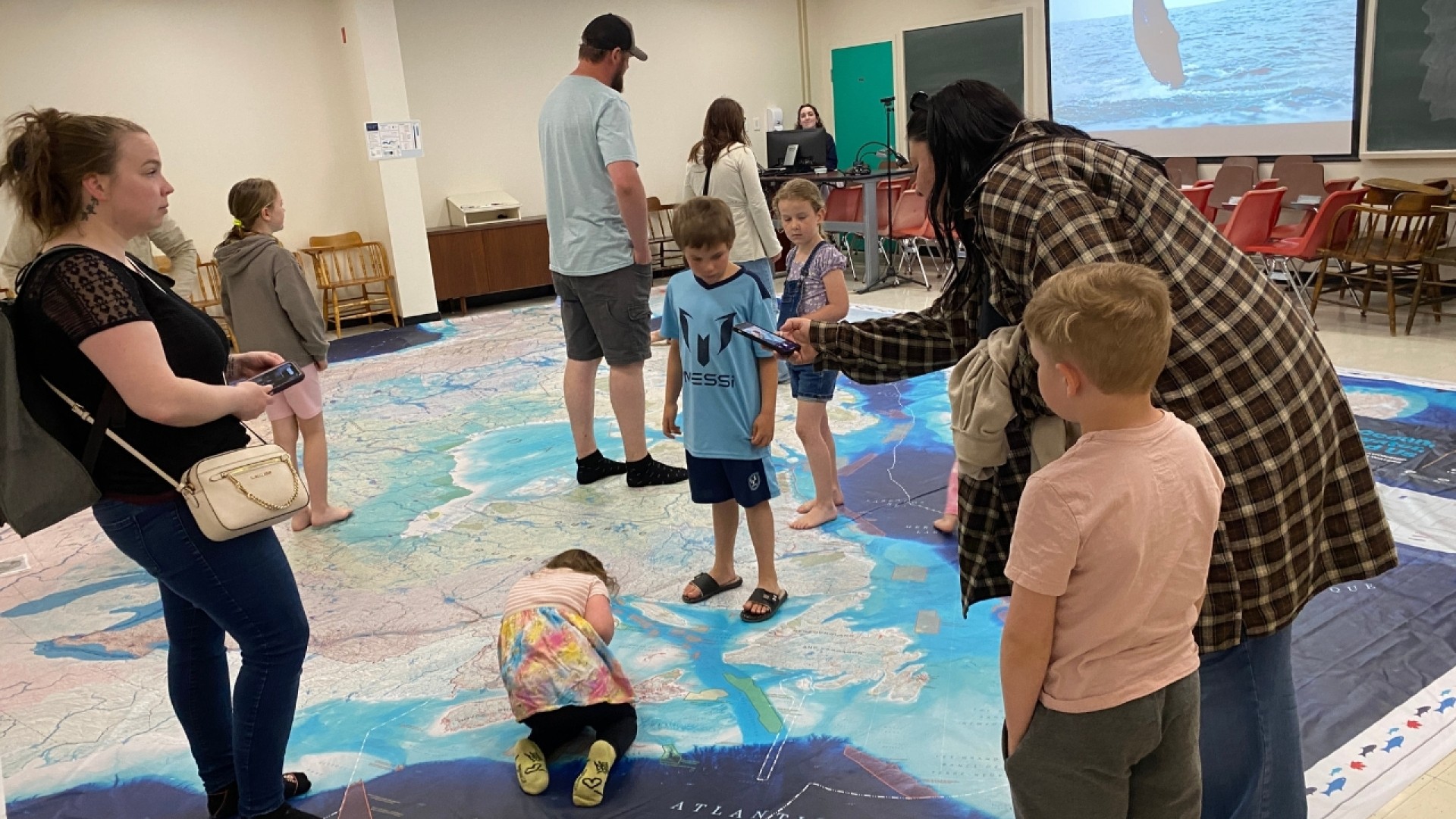 Children and adults interacting on a large floor map of Canada in a classroom setting