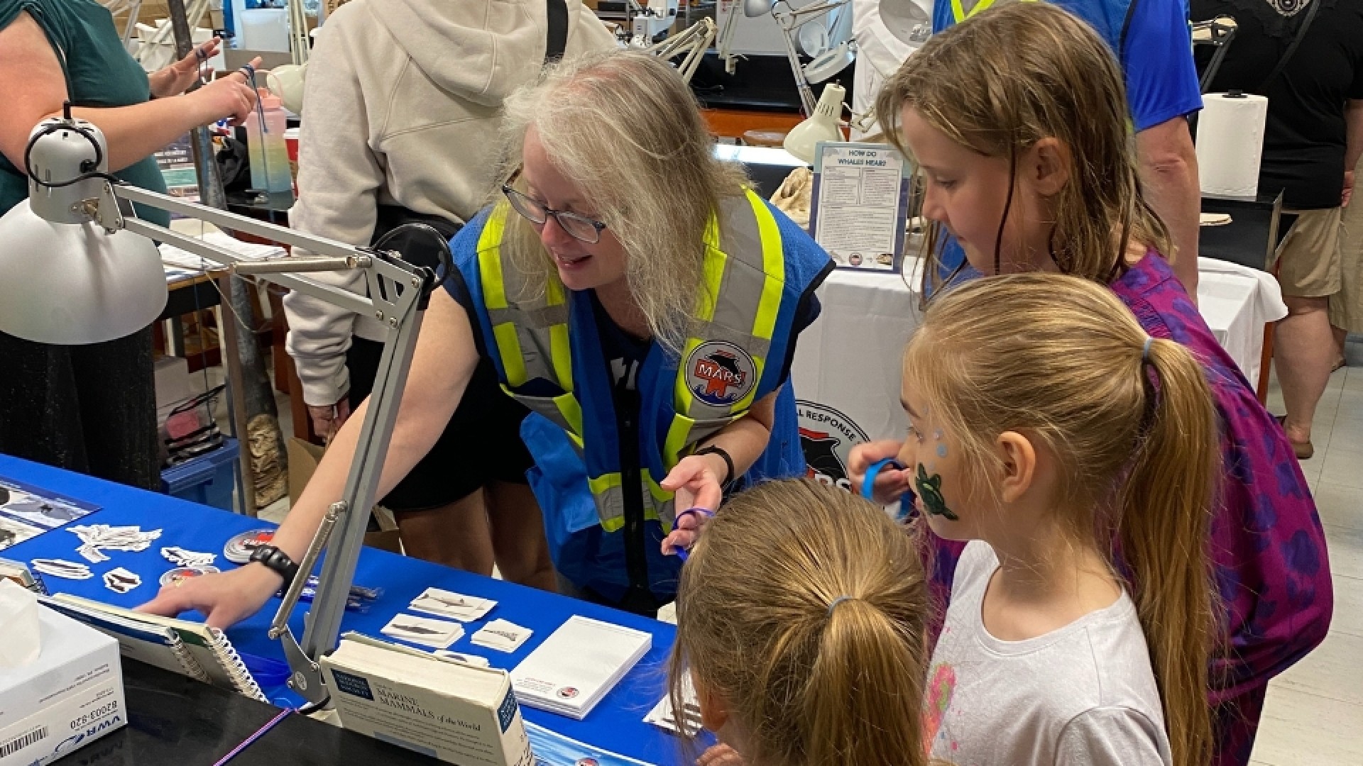 Children and adults gathered around a display table at an indoor event