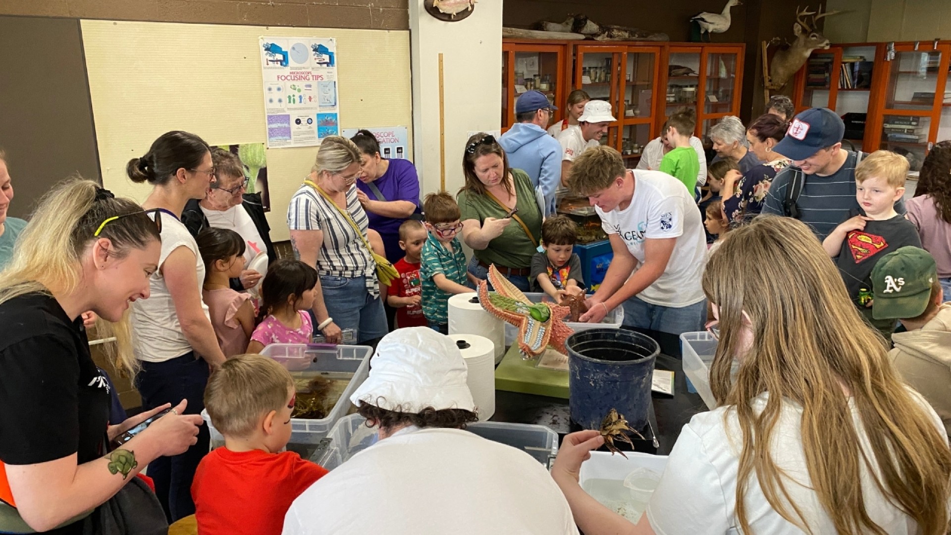 Children and adults gathered around tables with containers and educational materials at a hands-on learning event.