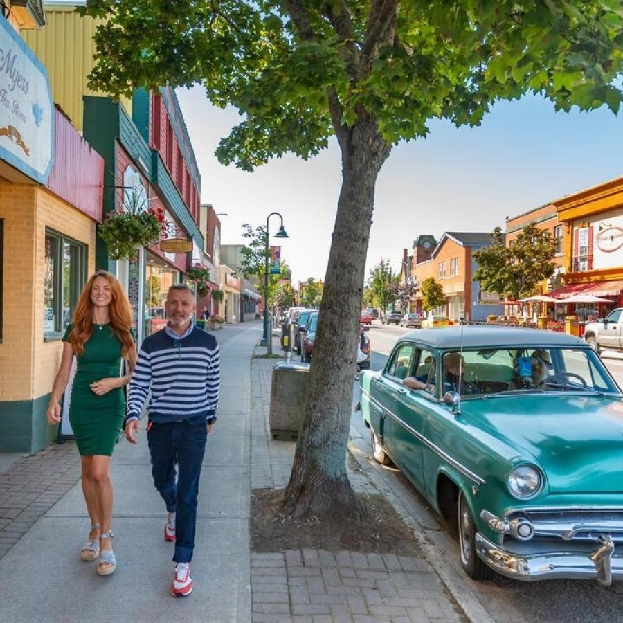 A woman and a man walking down Main Street, Downtown Antigonish. They're walking past Myers Tea Room with a teal vintage car parked on the street.