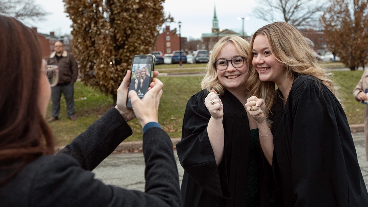 Two women pose next to each other holding up their X-Rings outside of the Keating Centre as another woman takes a photo of them on a phone.