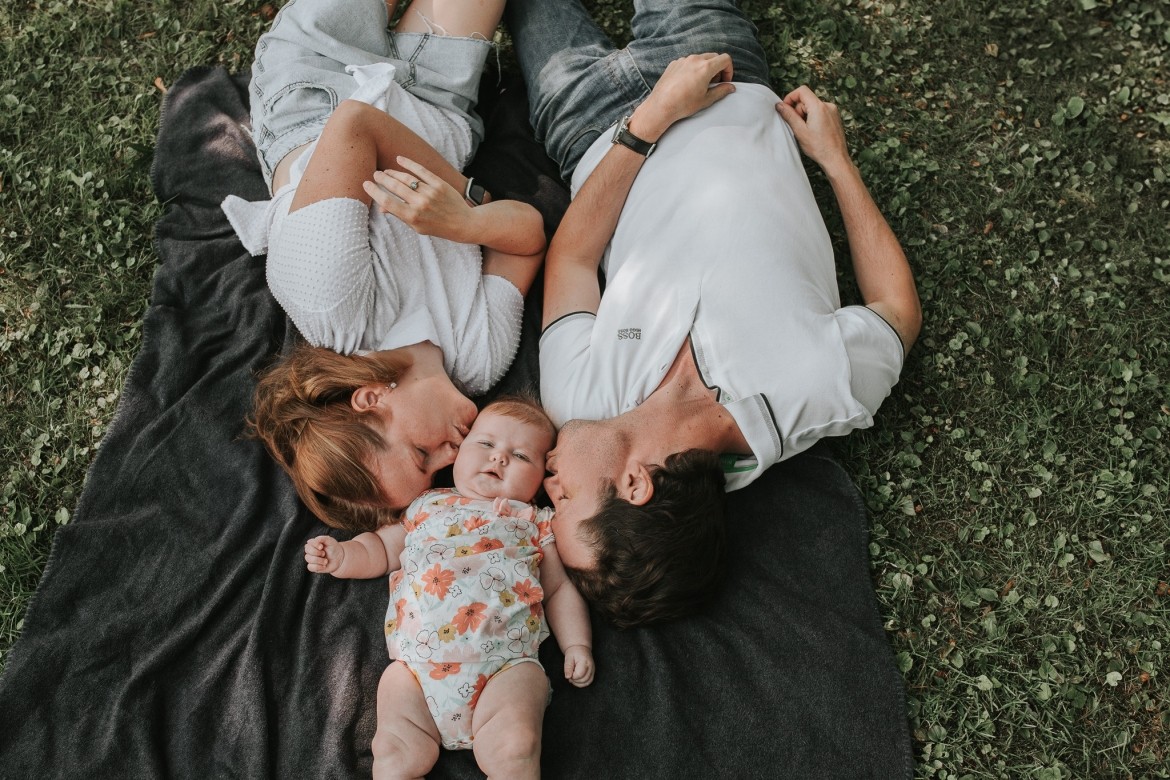 Parents lying on a blanket outdoors with their baby