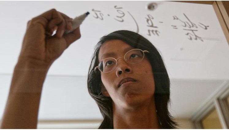 A student is writing math formula on the transparent glass board.