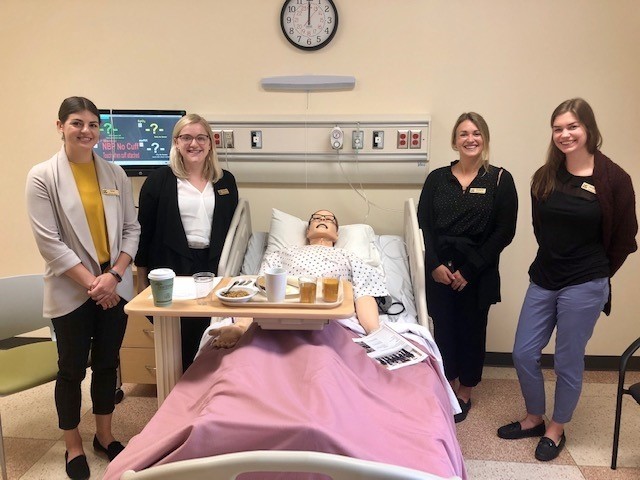 4 Nurses standing around dummy patient in hospital bed
