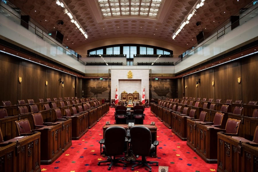 Dark wood-panelled room with rows of chairs and red carpet down the middle.