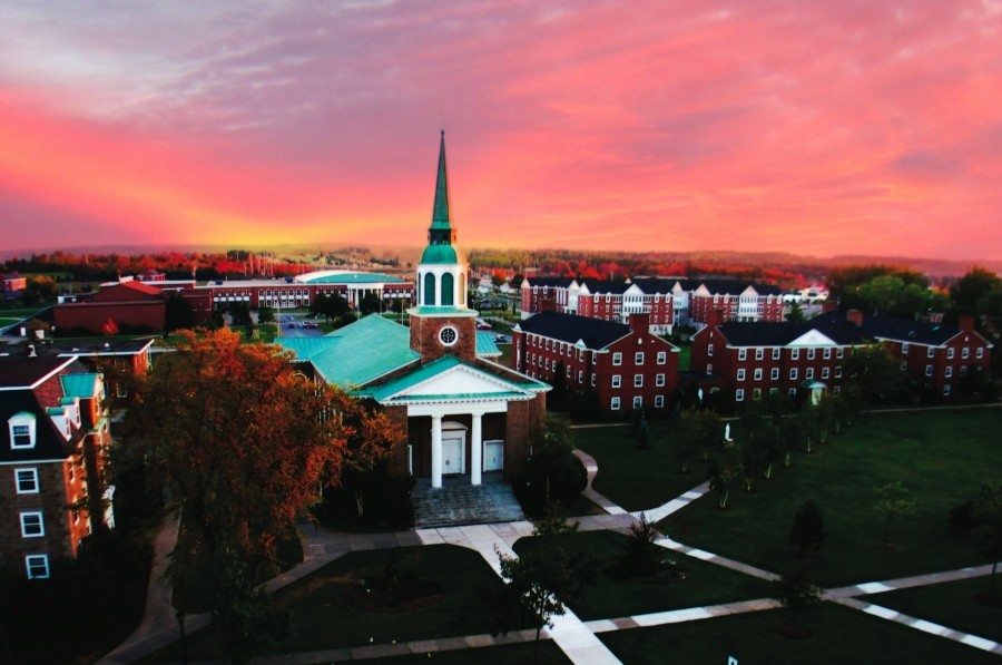 A church surrounded by campus buildings with a pink sunset
