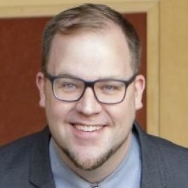 A person smiling wearing glasses and a tie